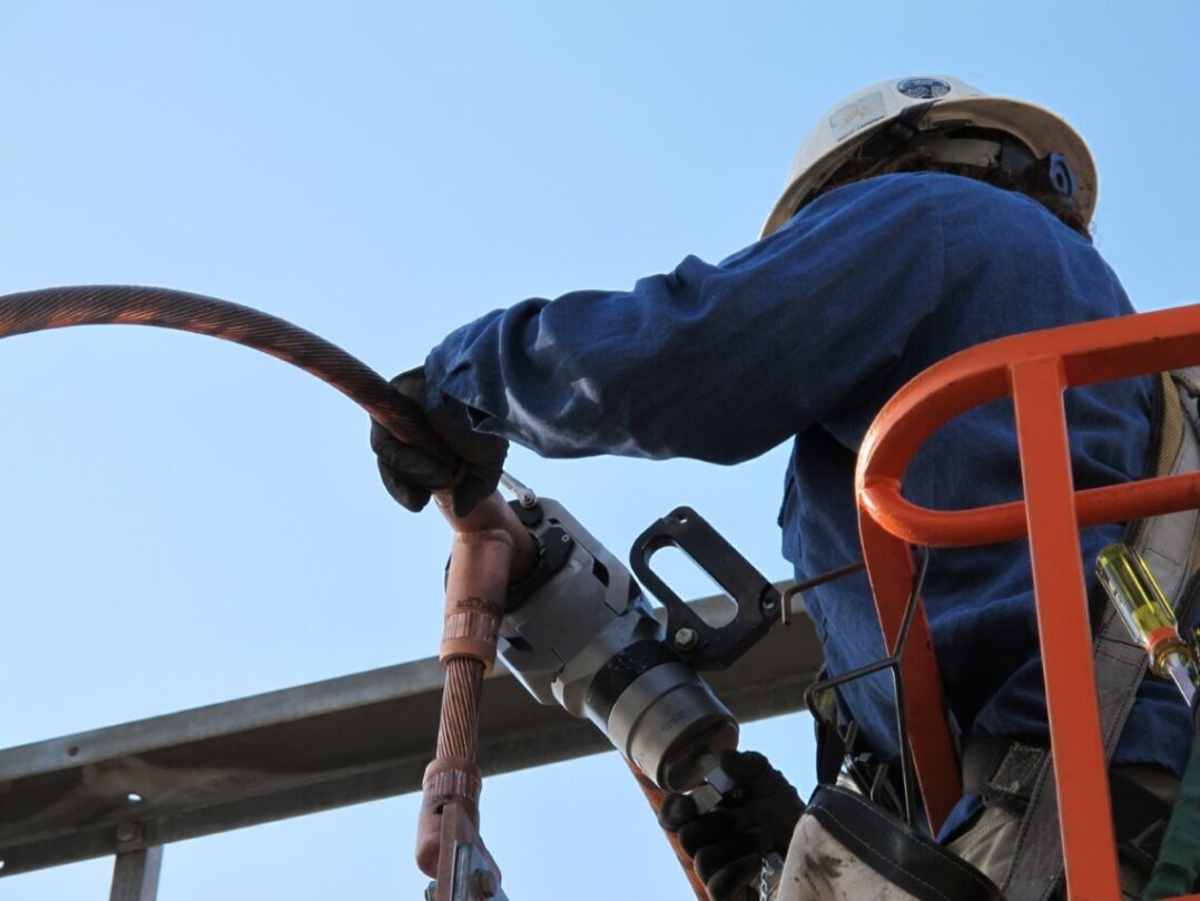 Utility worker in basket using DMC Power tooling on an electrical connector, ensuring secure connections